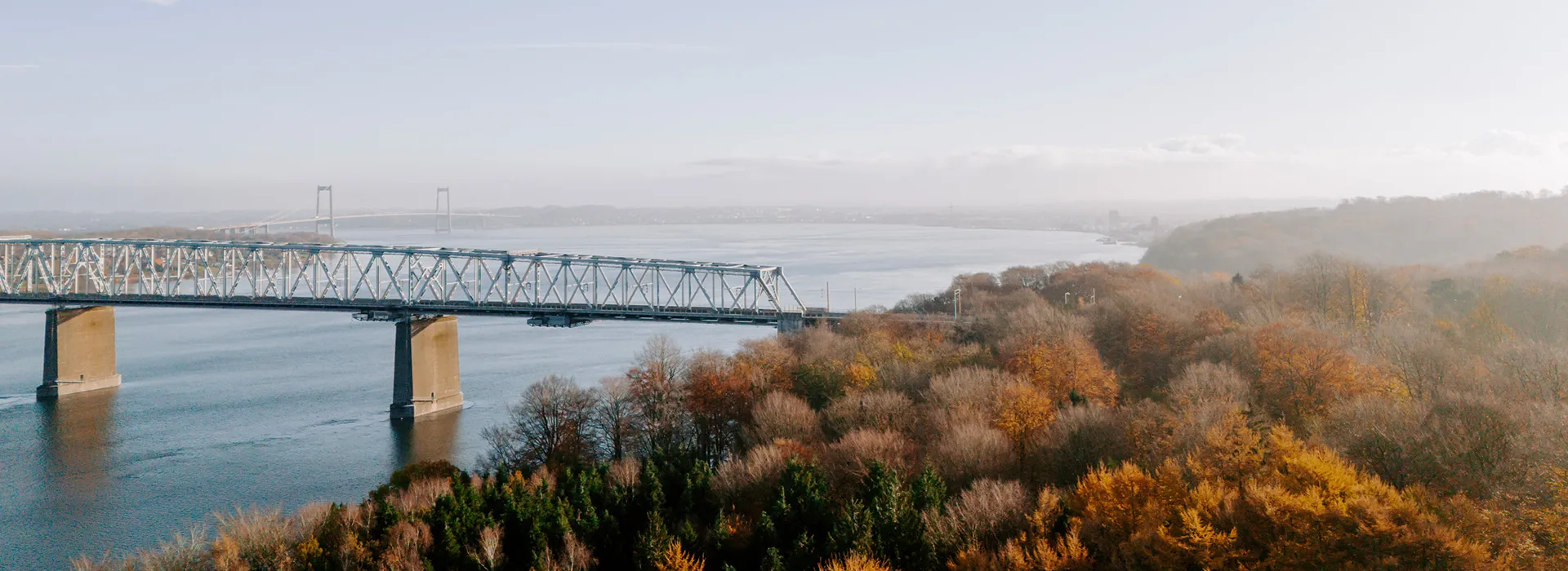 Den gamle Lillebæltsbro set fra oven med efterårsfarvet skov og stille vand
